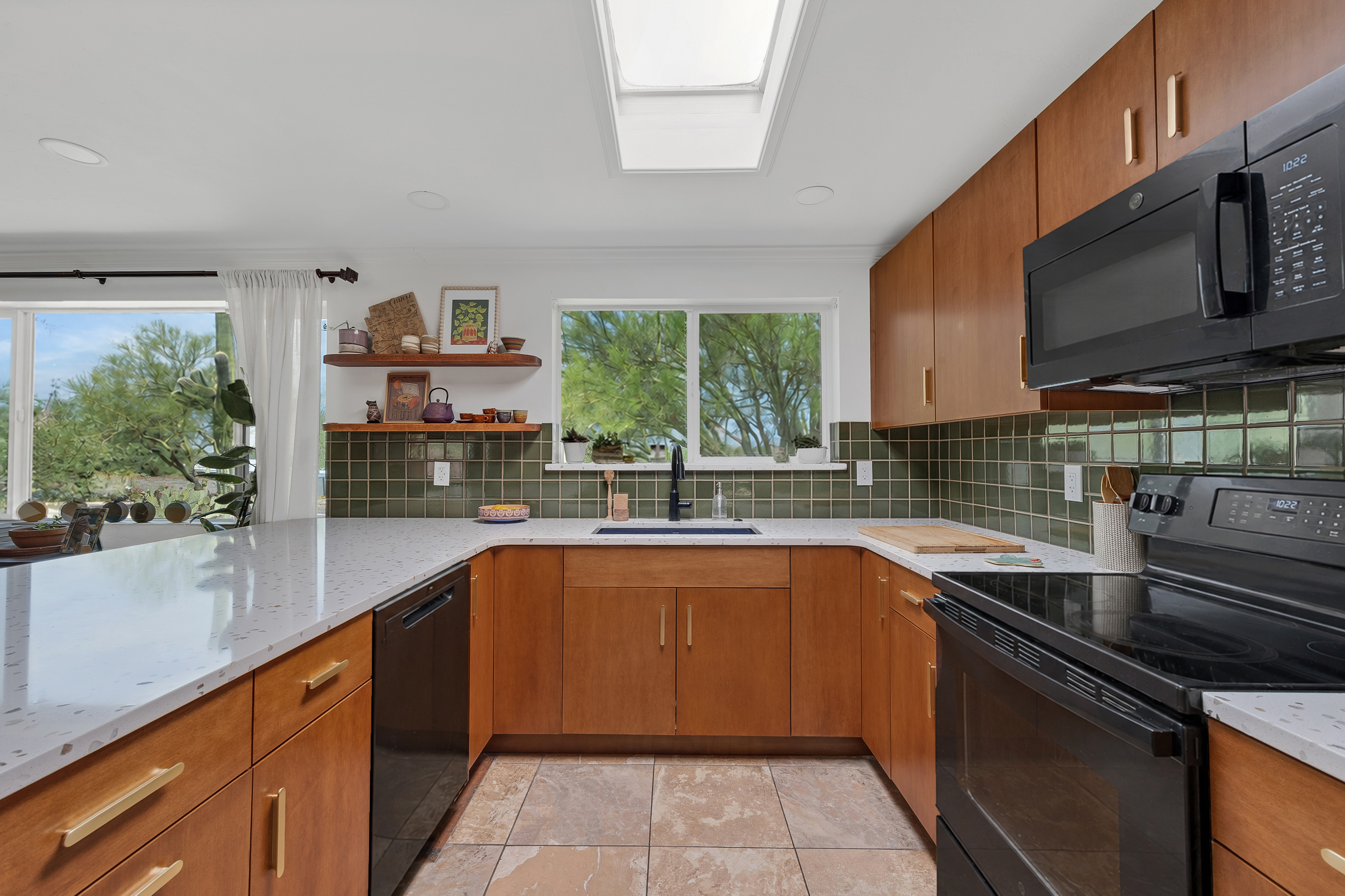 Modern Oro Valley kitchen remodel with warm wood cabinetry, green tile backsplash, floating shelves, and upgraded black appliances.