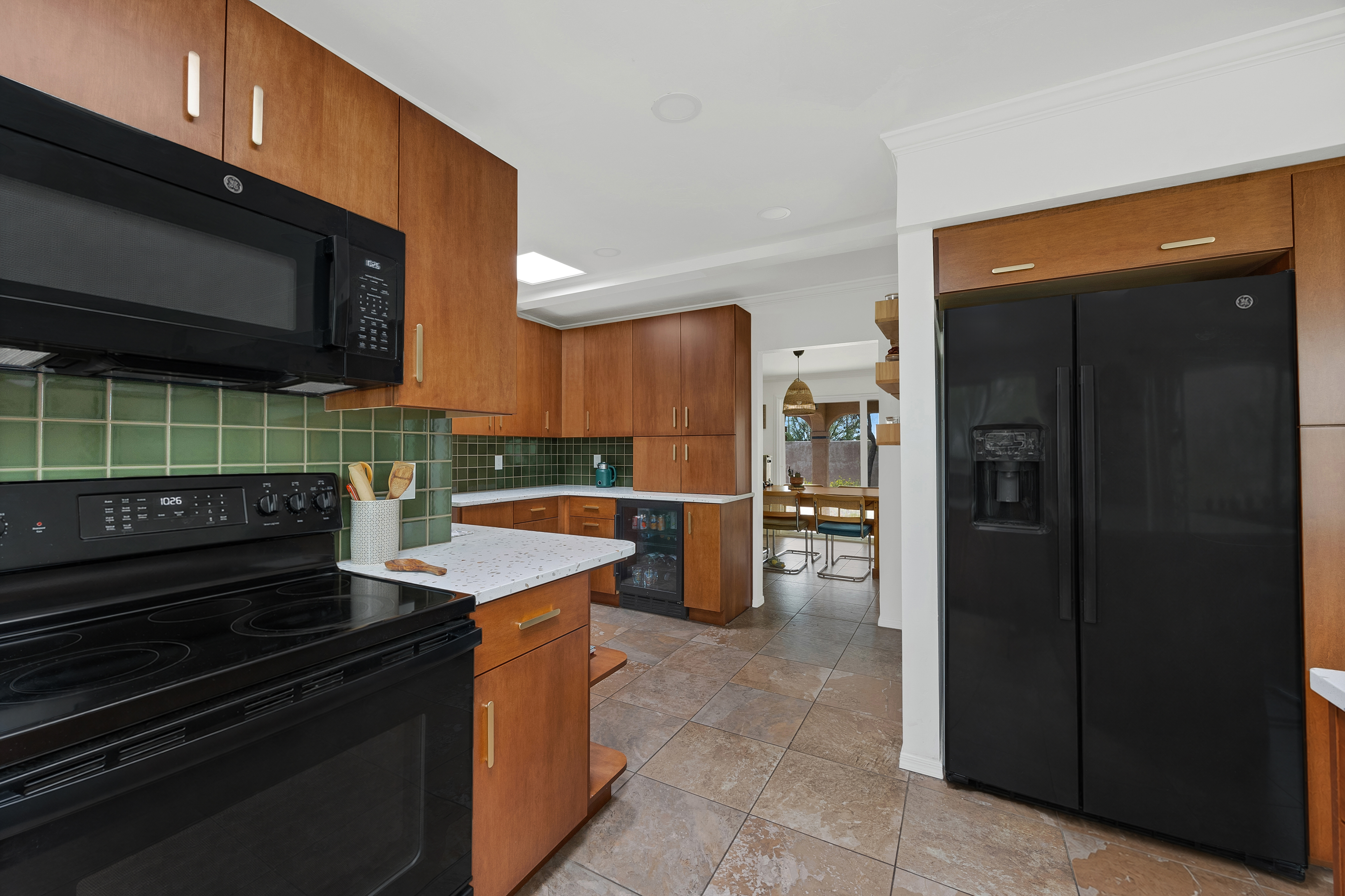 Modern kitchen remodel with warm wood cabinets, green tile backsplash, black appliances, and a view into the dining area.