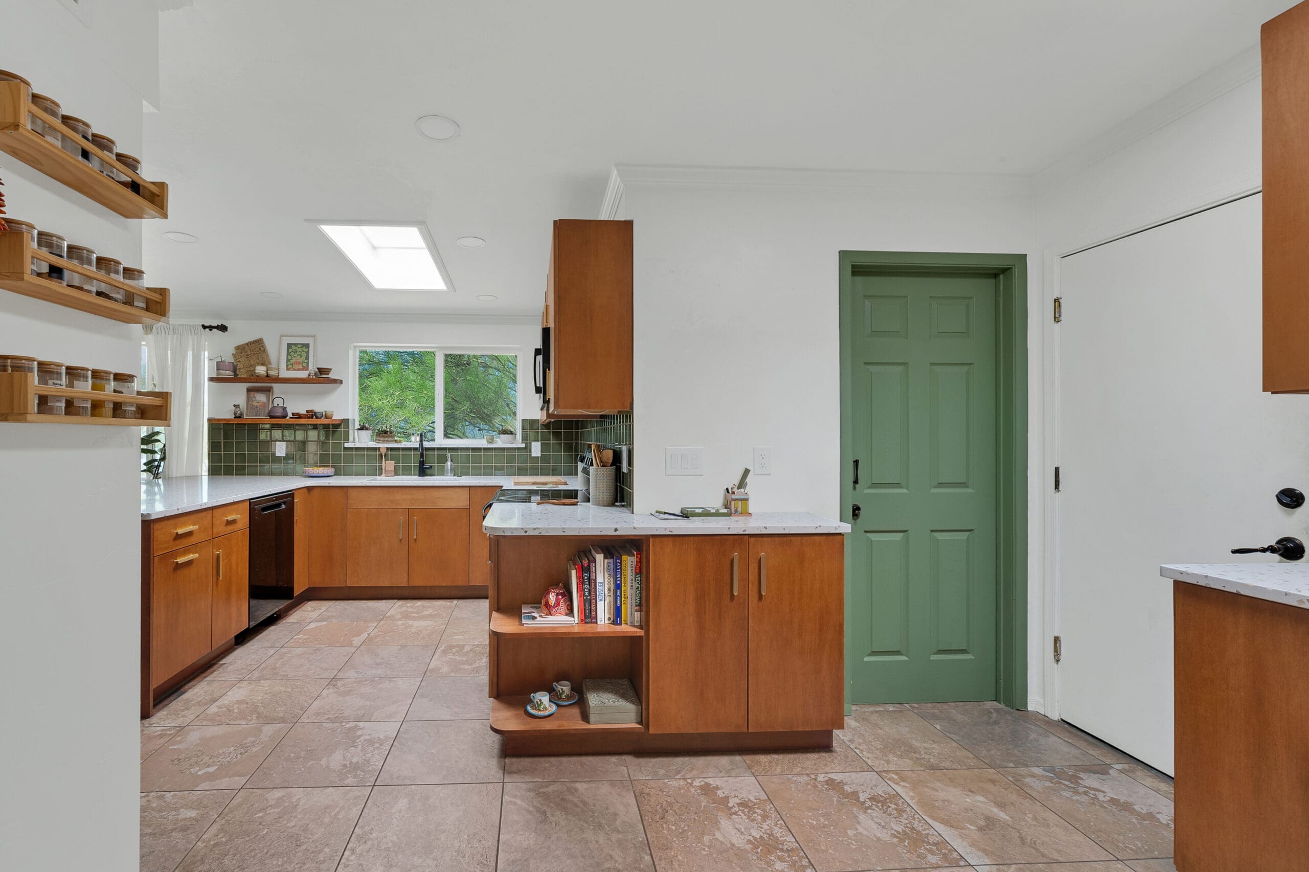 Modern kitchen remodel with warm wood cabinets, green tile backsplash, open shelving, and a green accent door.