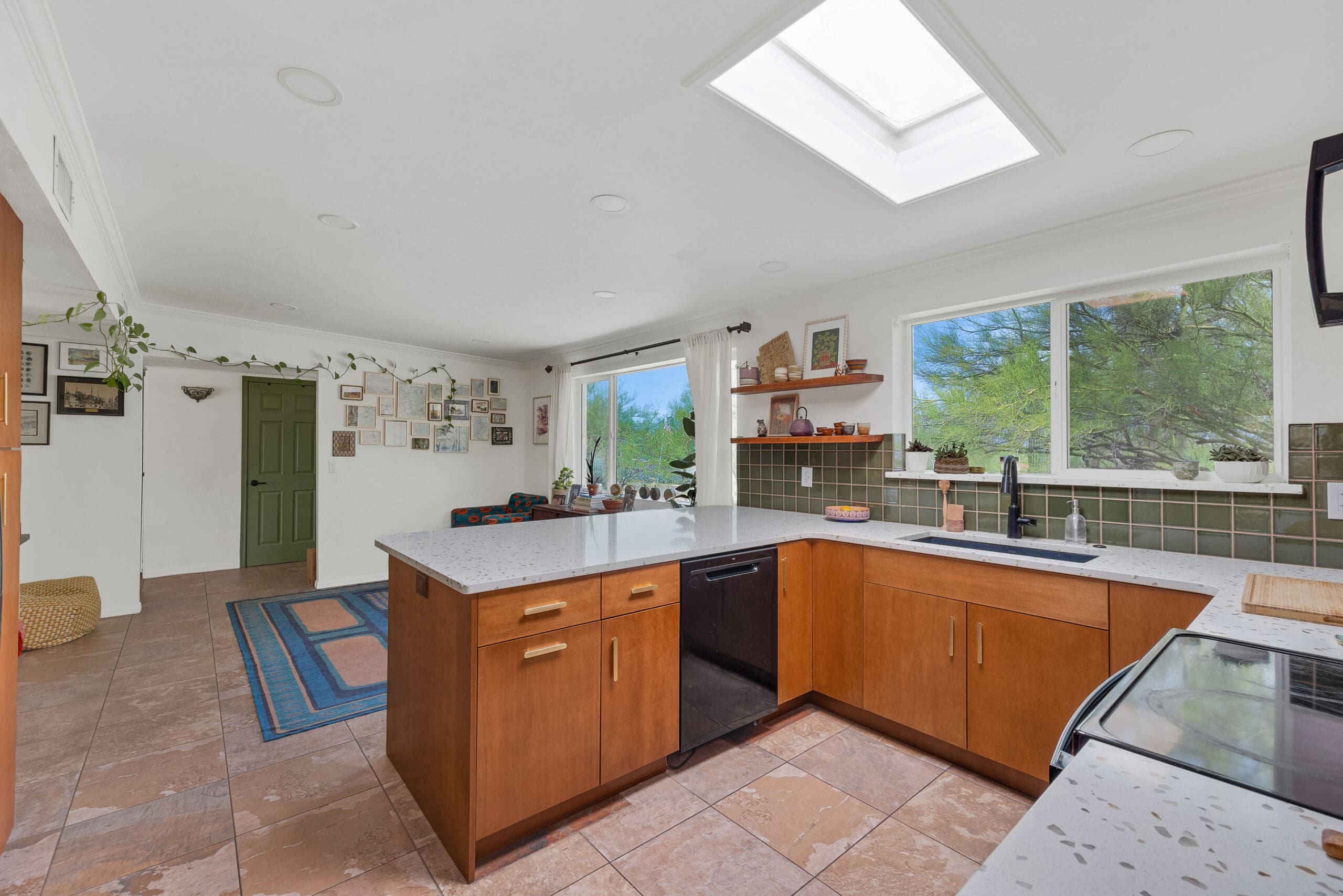 Open‑concept kitchen and living area remodel with wood cabinetry, green tile backsplash, skylight, and modern Southwest décor.