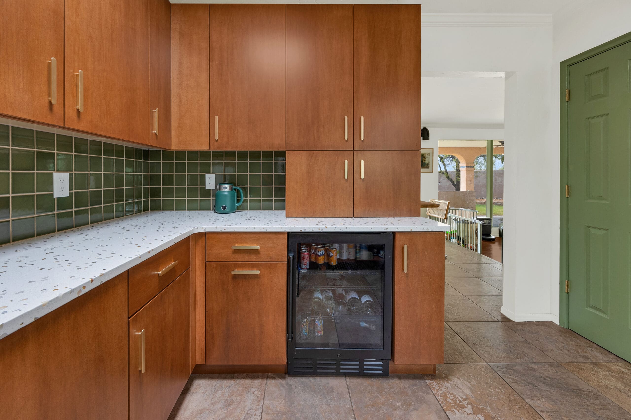 Modern kitchen remodel with wood cabinetry, green tile backsplash, beverage fridge, and open view to dining and patio areas.