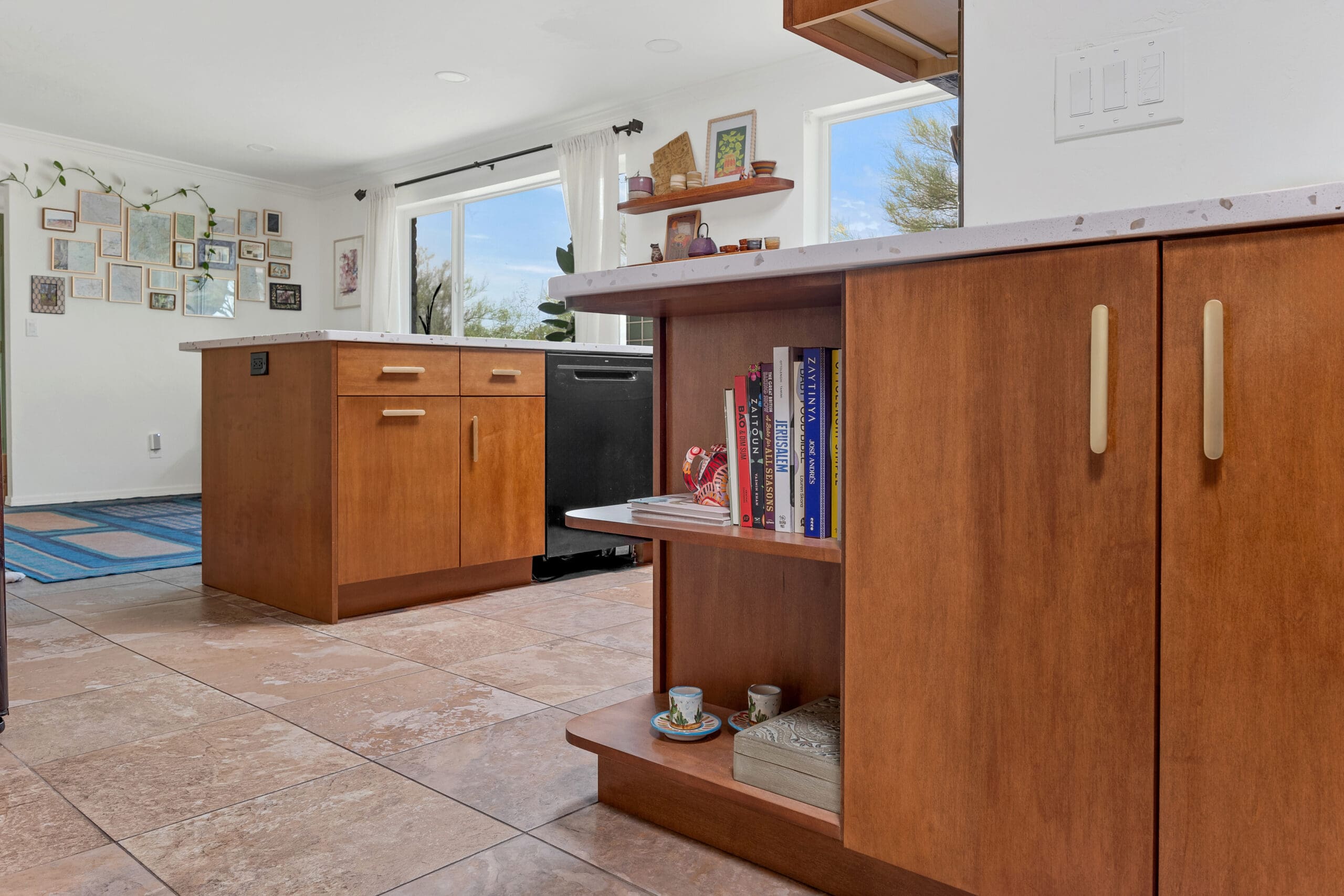 Modern kitchen remodel with wood cabinetry, built‑in shelving, terrazzo‑style island countertop, and bright natural light.