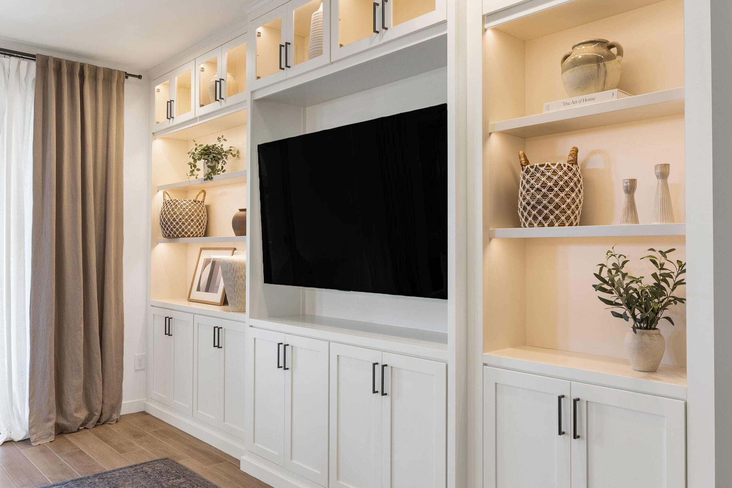Custom white built‑in entertainment unit with Bertch cabinetry, integrated lighting, open shelves styled with décor, and a centered TV in a modern Tucson living room.